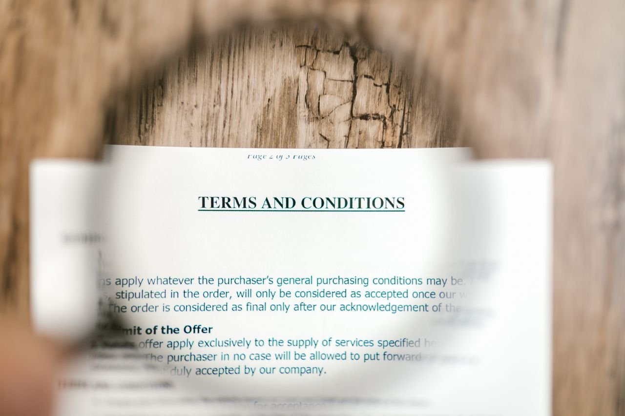 About Magnifying glass focusing on terms and conditions document on wooden surface.