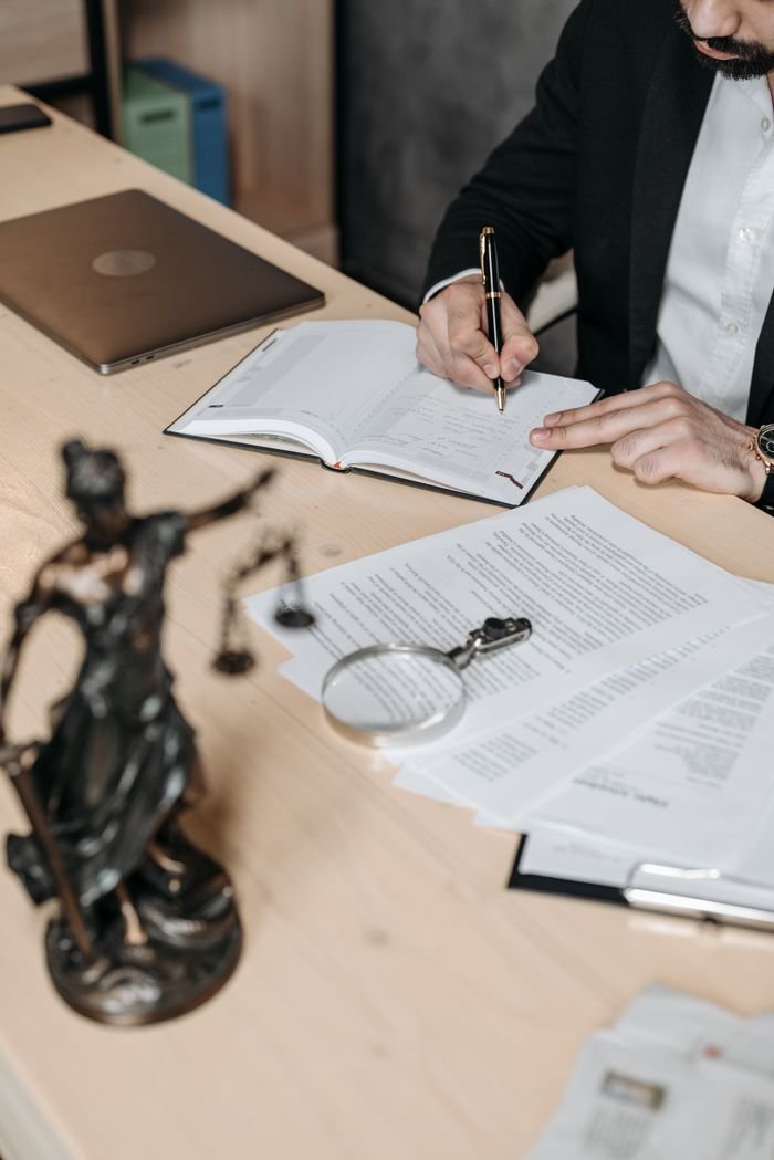 Services Professional working on documents at desk with legal statue and magnifying glass.
