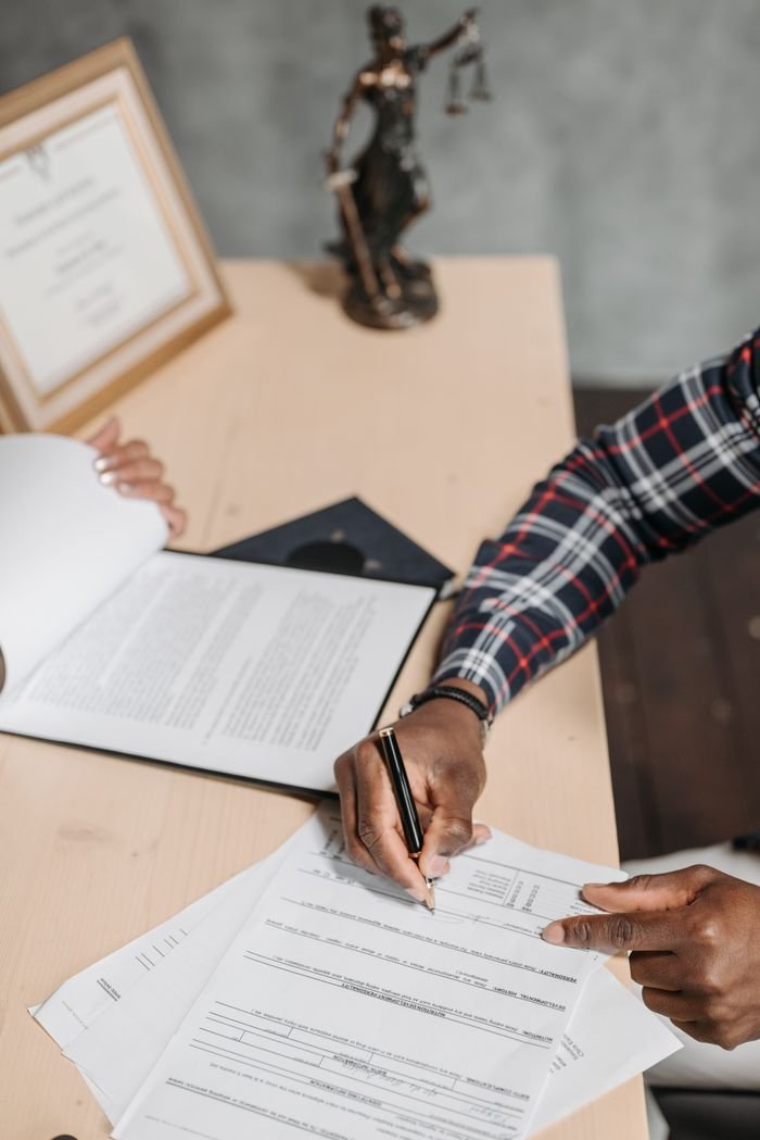 Services Hands of a person signing official documents on a desk in an office setting.